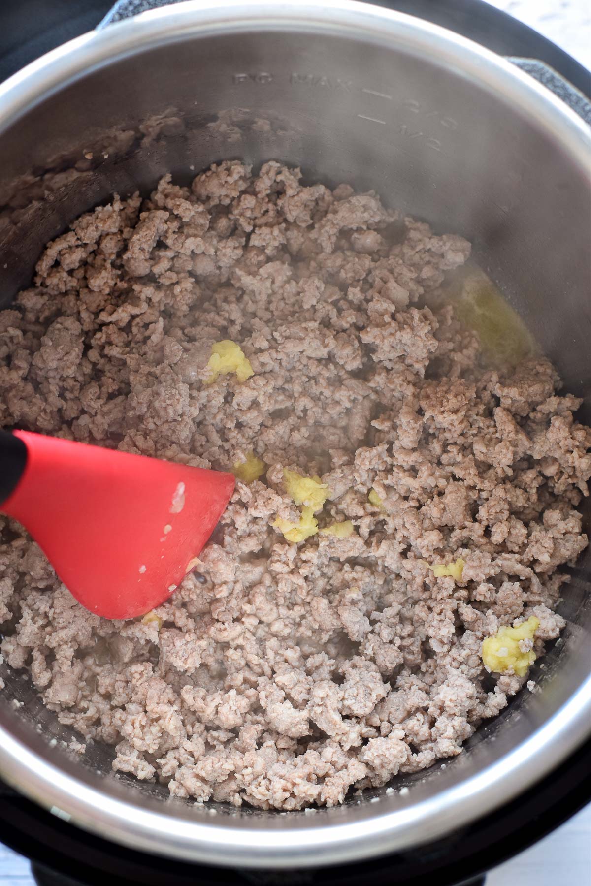 shredded garlic being sauteed with browned ground pork in an instant pot with a red spatula.