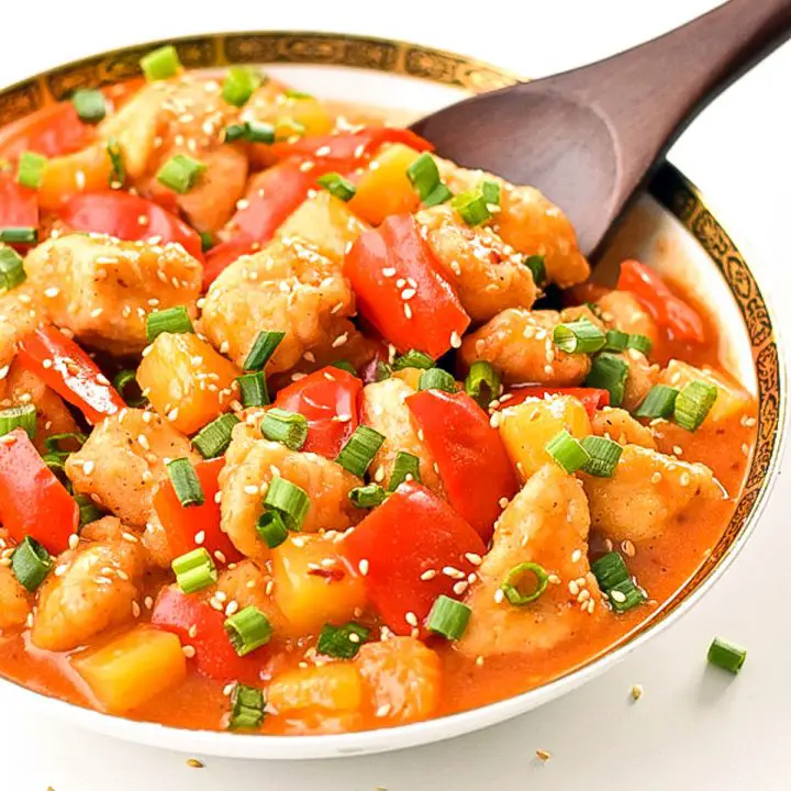 a bowl of gluten-free sweet and sour chicken with a wooden spoon.