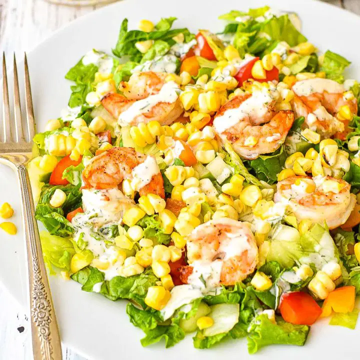 close-up of summer detox salad with grilled shrimp, corn, bell peppers, and lettuce dressed in dairy-free ranch dressing on a white plate with a fork.